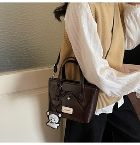 Side view of dark brown tote bag with bear charm and heart pendant on a model