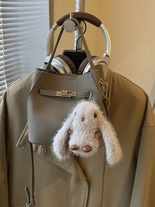 Grey textured leather bucket bag with silver buckle and plush bunny charm on trench coat