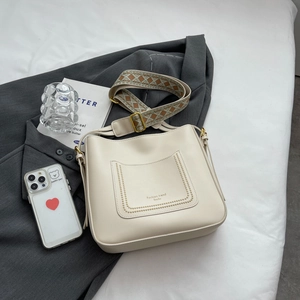 Sac seau blanc cassé avec bandoulière ethnique posé sur une veste grise chic
