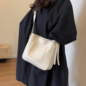 Sac seau blanc avec lettrage doré et bandoulière tressée porté sur manteau noir