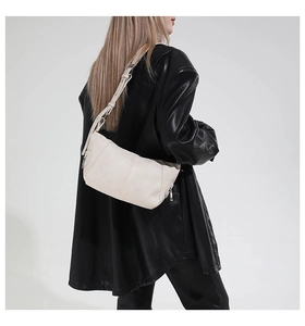 Detail view of a cream leather crescent shoulder bag with pebbled texture and metal hardware