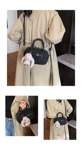 Detail of black leather satchel with decorative buckle and plush bunny charm on a coat