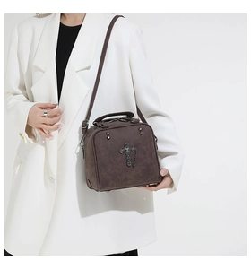 Detail of dark brown vintage pillow bag with gothic cross and chain on white suit background