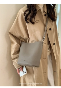 Detail of gray bucket bag featuring lychee texture and adjustable strap on a model