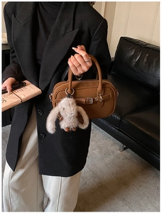 Close-up of brown matte tote bag with strap buckle and plush rabbit keychain detail