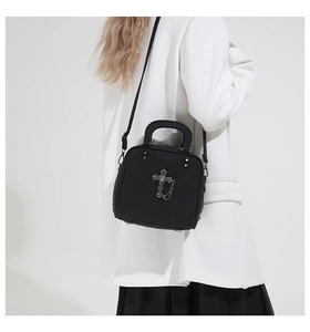 Detail of black matte handbag featuring silver gothic cross and chain on model