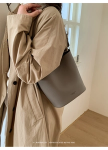 Close-up of taupe lychee texture leather bucket bag with slim shoulder strap on model