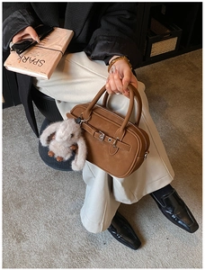 Detail of a brown leather Boston bag featuring a belt buckle and soft plush rabbit charm