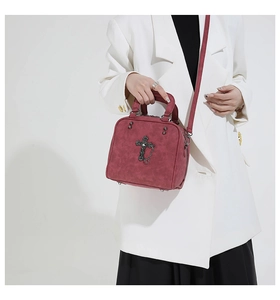 Detail of burgundy crossbody bag with baroque metal cross and stud embellishments