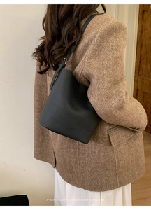 Detail view of black lychee grain leather bucket bag on shoulder with retro vibe