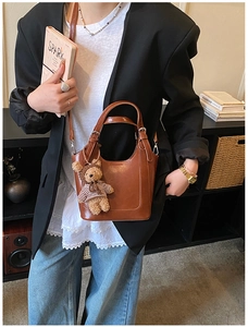 Brown bucket bag with dual handles and cute plush bear charm in a lifestyle interior setting