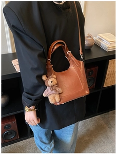 Close-up of brown PU leather bucket bag featuring a cute teddy bear charm and adjustable strap