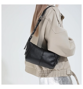 Close-up of black pebbled leather baguette bag with stitching and adjustable metal eyelet strap