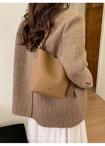 Detail of camel retro bucket bag with embossed logo worn by model in wool blazer