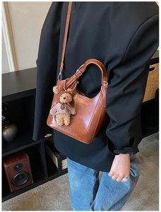 Close-up of brown vintage leather bucket bag featuring a cute striped bear pendant