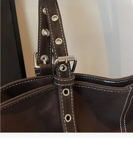 Détail du sac en cuir marron foncé avec œillets argentés et coutures contrastées blanches