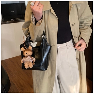 Chic black bucket bag with teddy bear pendant shown on model in khaki trench coat