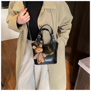 Chic black bucket bag with glossy finish and cute teddy bear charm on beige trench coat