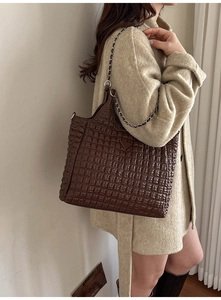 Detail of dark brown quilted tote bag with triangle logo and chain strap on shoulder