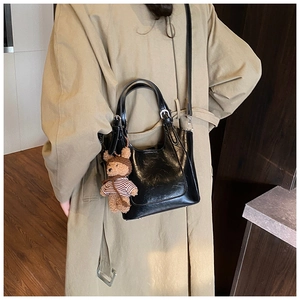 Detail of black glossy bucket bag with a cute bear charm on a khaki trench coat