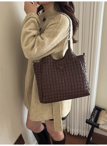 Detail of dark brown quilted tote bag with metal triangle logo and chain strap