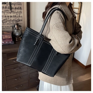 Detailed view of black tote bag with white contrast stitching and braided strap handle