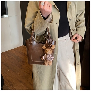 Close-up of a brown leather bucket bag with a plush bear charm on a trench coat model