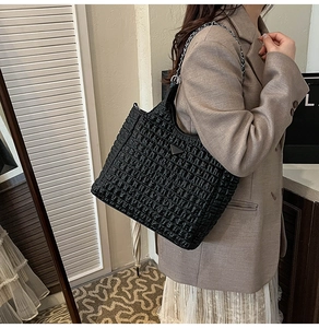 Detail of black pleated texture tote bag with silver chain strap and metallic triangle