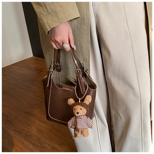 Detail of dark brown leather bucket bag with teddy bear charm and metal buckle accents