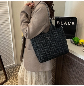 Macro detail of quilted black leather tote with metal triangle logo and chain strap