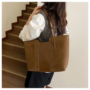 Detail of a large brown tote bag with white contrast stitching and woven side accents