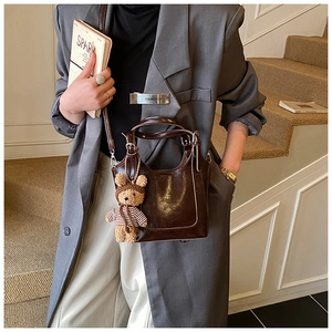 Model showcasing a dark brown leather bucket bag with a cute bear charm on stairs