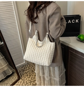 Detail of white quilted tote bag featuring silver chain handle and iconic triangular logo