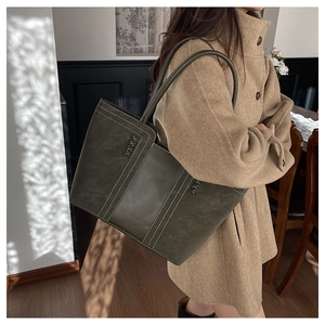 Deep green tote bag featuring contrast stitching and leather straps in a home setting
