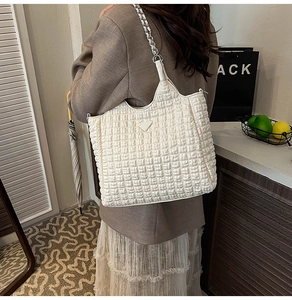 Detail of white quilted tote bag with silver chain strap and signature triangle emblem