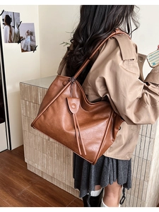 Close-up of a brown soft leather tote bag with tassel detail on a woman's shoulder