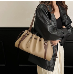 Detail of beige shoulder bag featuring ruched drawstring top and brown leather strap