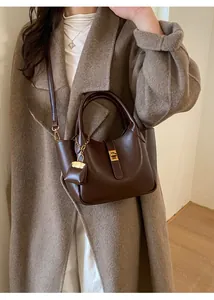 Detail of dark brown leather handbag with gold metal lock and hanging charm accessory