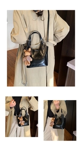 Detail of black glossy bucket bag with long shoulder strap and cute plush bear charm