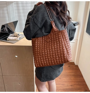 Close-up of brown quilted tote bag with chain strap and glossy texture on wood desk