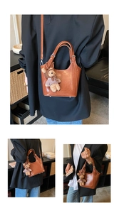 Detail view of brown leather bucket bag with a cute bear charm and adjustable straps