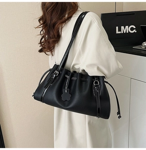 Detail of black pleated leather tote bag with drawstring closure and cloud charm on shoulder