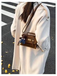 Outdoor shot of a brown vintage satchel with metal buckle and cute teddy bear charm