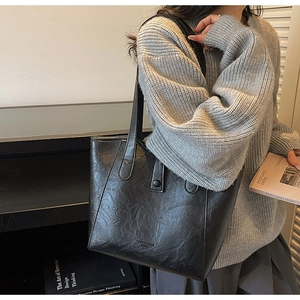 Detail view of black vintage leather tote bag with natural texture shown with a grey sweater