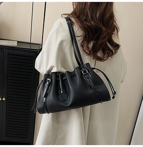Detail of black pleated leather tote bag featuring a floral charm and drawstring closure
