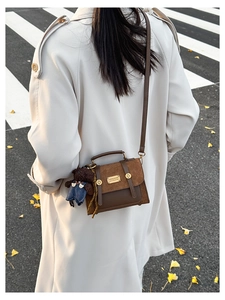 Brown vintage messenger bag with suede texture and cute teddy bear charm on street