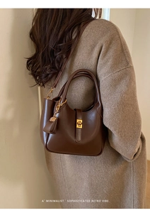 Detail of dark brown leather handbag with gold twist lock on a minimalist coat