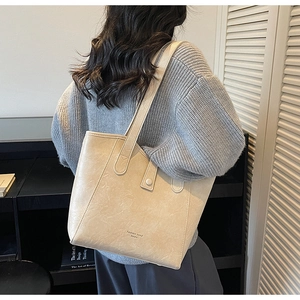 Detailed side view of the cream tote bag worn by a model in a minimalist interior setting