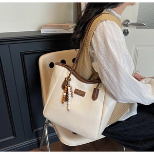 Detail view of cream tote bag with brown contrast trim and colorful wooden bead tassel charm
