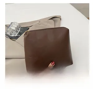 Dettaglio di una pochette in pelle smerigliata marrone scuro con cerniera d'oro